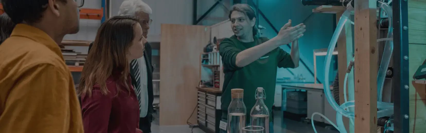 An Aquabattery employee showcases its acid-base flow battery technology to two men and two women in an industrial lab setting. 