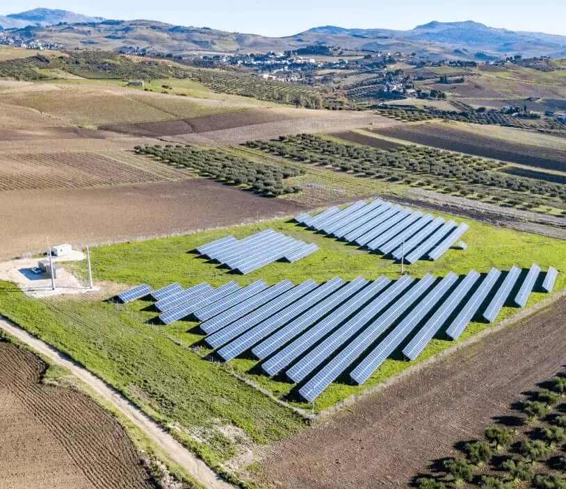 A solar farm installation with multiple, interconnected solar panels in a field surrounded by agricultural land.